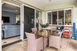 Una habitación con puerta de cristal que da a un balcón, una mesa de comedor con sillas de mimbre y un sofá al fondo.