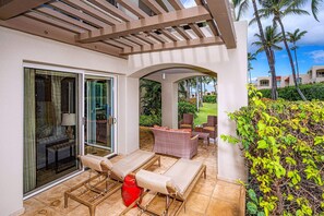 A covered outdoor seating area with a table and chairs, a red stool, and a glass door leading to an interior space.
