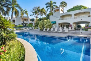 A swimming pool with lounge chairs and palm trees, surrounded by buildings with balconies.
