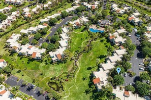 Vista aérea de una zona residencial con varias casas de dos pisos, un área central ajardinada con piscina y un estacionamiento.