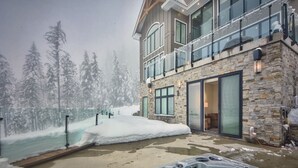 A multi-story building with a stone facade, large windows, and a balcony with snow. - RMR: Luxury Ski-in/out Mountain-side 4 Bedroom Home (Sleeps 10).  (Revelstoke)