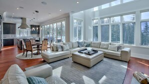 A spacious living room with a large sectional sofa, a dining area, and a kitchen with a view of the outdoors. - RMR: Luxury Ski-in/out Mountain-side 4 Bedroom Home (Sleeps 10).  (Revelstoke)