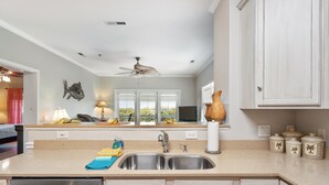 Une cuisine équipée d’un évier à deux bacs, d’un ventilateur de plafond et offrant une vue sur l’extérieur grâce à de grandes fenêtres.
