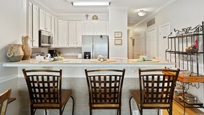 Une cuisine moderne avec des meubles blancs, un îlot central et un coin repas doté de chaises en bois.