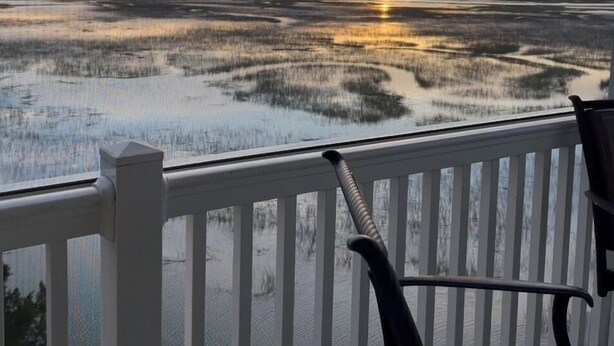 Vue depuis un balcon donnant sur une zone humide, avec un coucher de soleil en arrière-plan.