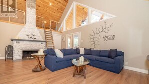 Un amplio salón con un sofá seccional azul grande, una chimenea y un área en altura con techo de madera.