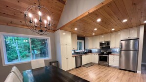 Una cocina moderna con pisos de madera, gabinetes blancos, electrodomésticos de acero inoxidable y un comedor amplio.