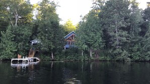 Una cabaña rodeada de un bosque frondoso, un muelle y un pequeño bote.