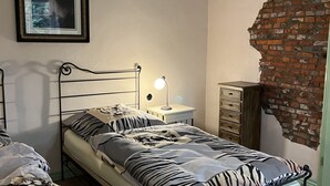 Una cama individual con una colcha de estampado de cebra, una mesita de noche con lámpara, y un cuadro en la pared.