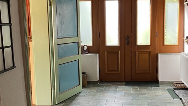 Una habitación con techo de madera, puerta verde y suelo de baldosas.
