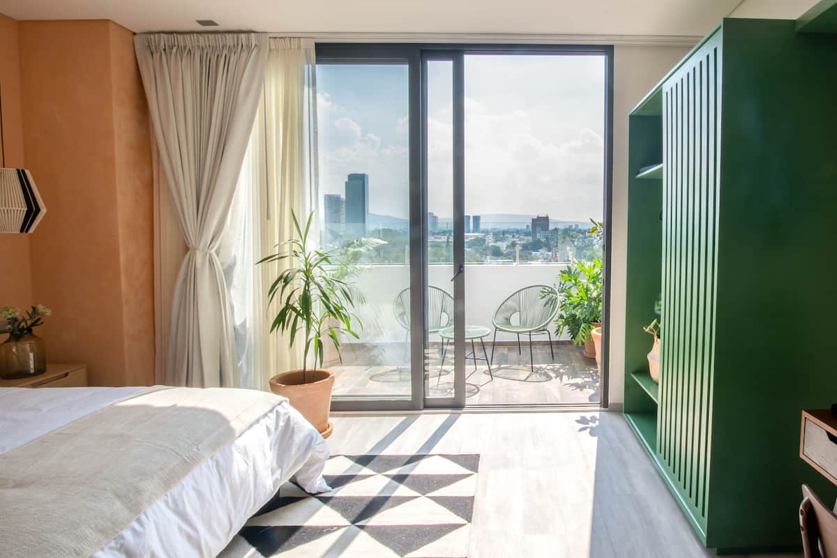 Une chambre moderne avec un grand lit, un balcon avec des chaises et une vue sur la ville.