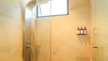 A shower with a curved showerhead, a small window, and a shelf with two bottles of Vervan shampoo.