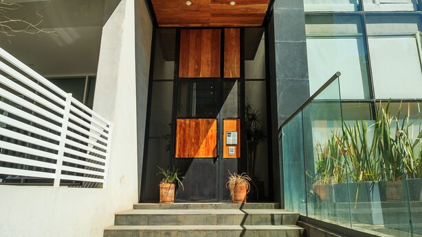 Entrada moderna de un edificio con diseño de paneles de madera, puerta de cristal y plantas en macetas en los escalones.