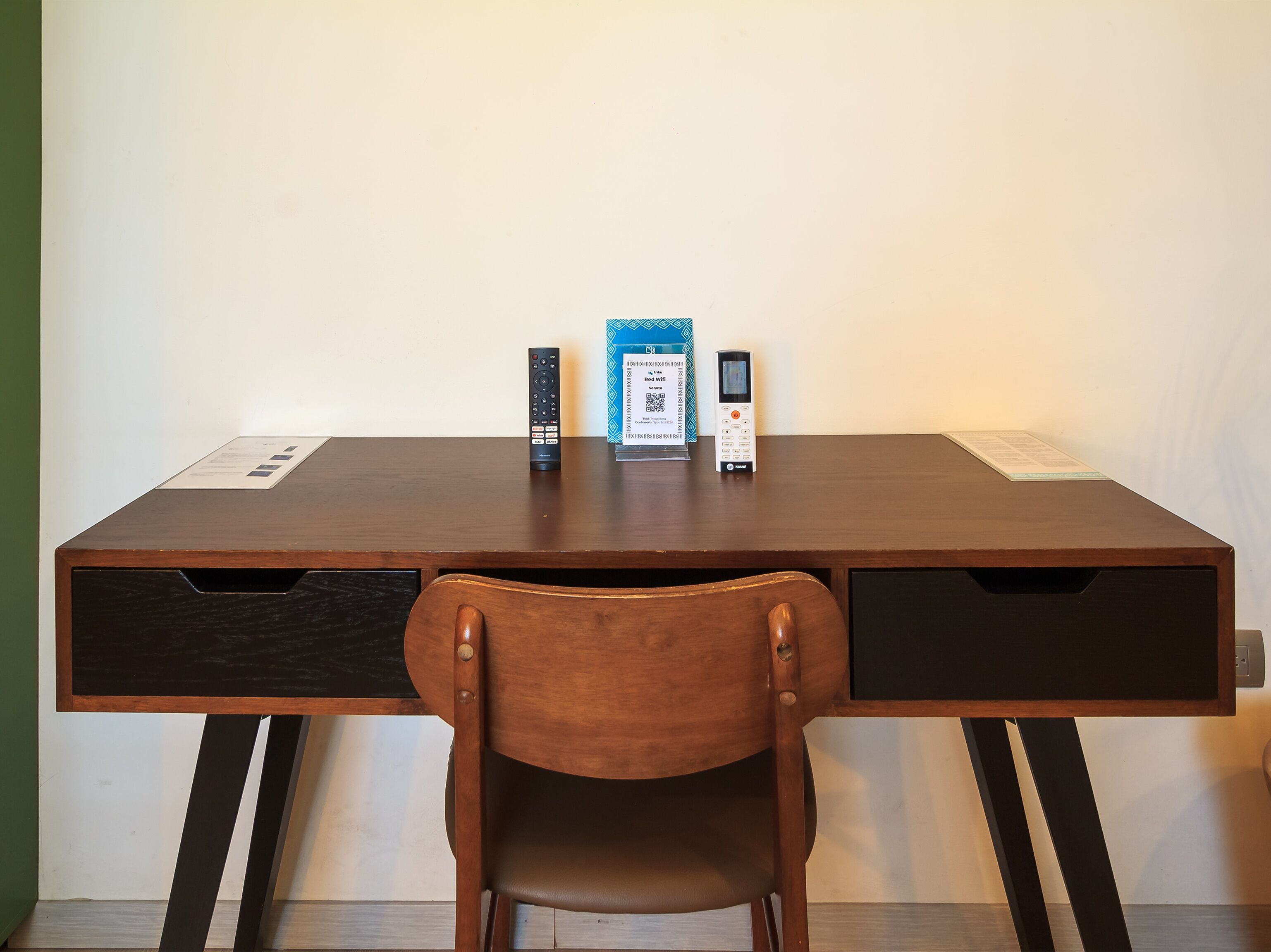 A wooden desk with two drawers, a chair, and two remote controls on the desk.