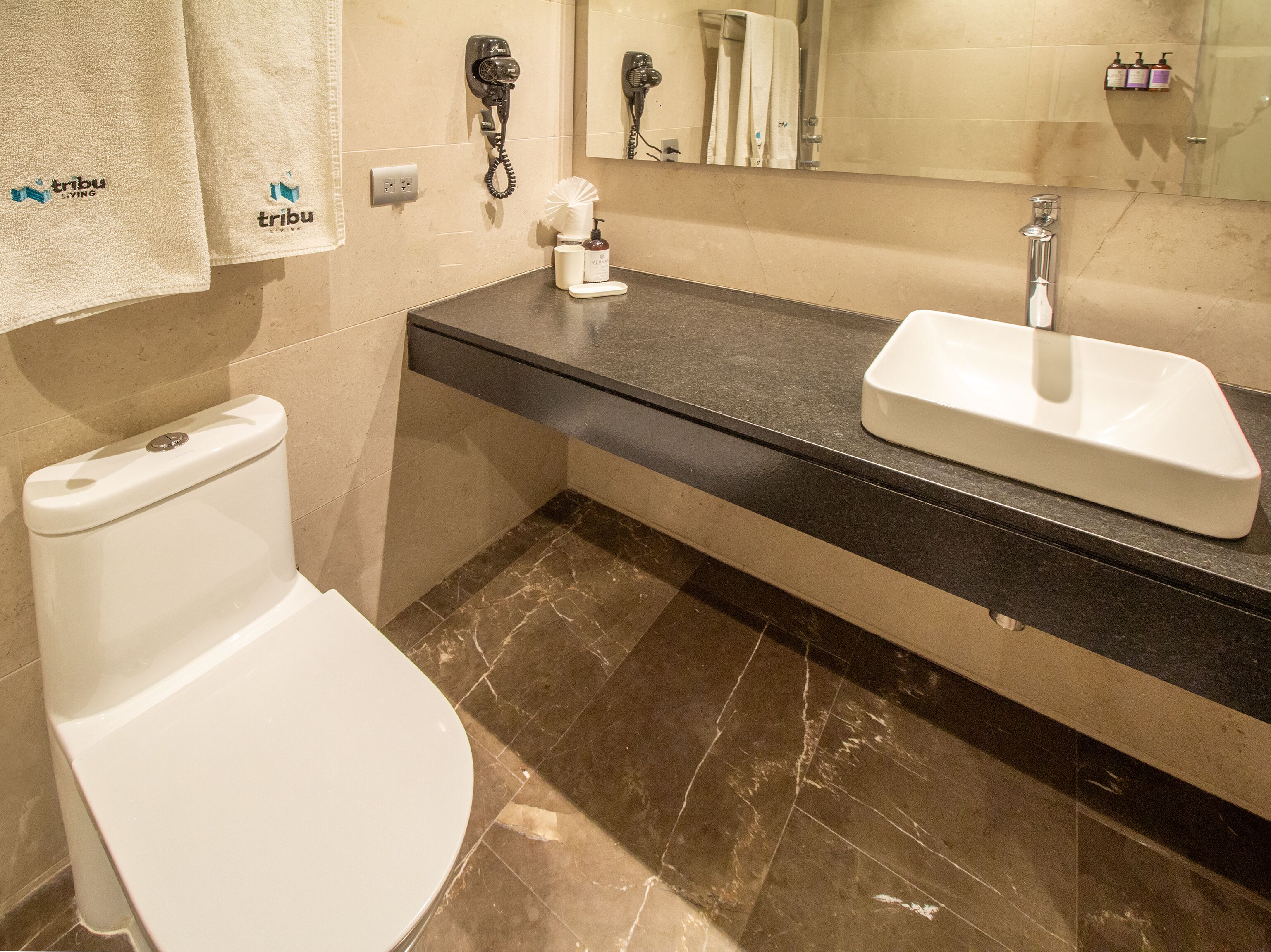 Ein Badezimmer mit Toilette, Waschbecken und Spiegel. Handtücher hängen an der Wand und ein Föhn steht auf der Ablagefläche.