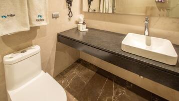 A bathroom with a toilet, a sink, and a mirror. There are towels hanging on the wall and a hairdryer on the counter.