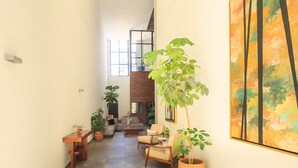 Un pasillo amplio con una escalera moderna, una zona de estar con sofás y sillones, y varias plantas en macetas.