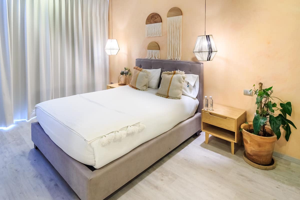 Un lit bien fait, avec une couette blanche, une table de chevet avec une lampe et une plante en pot.