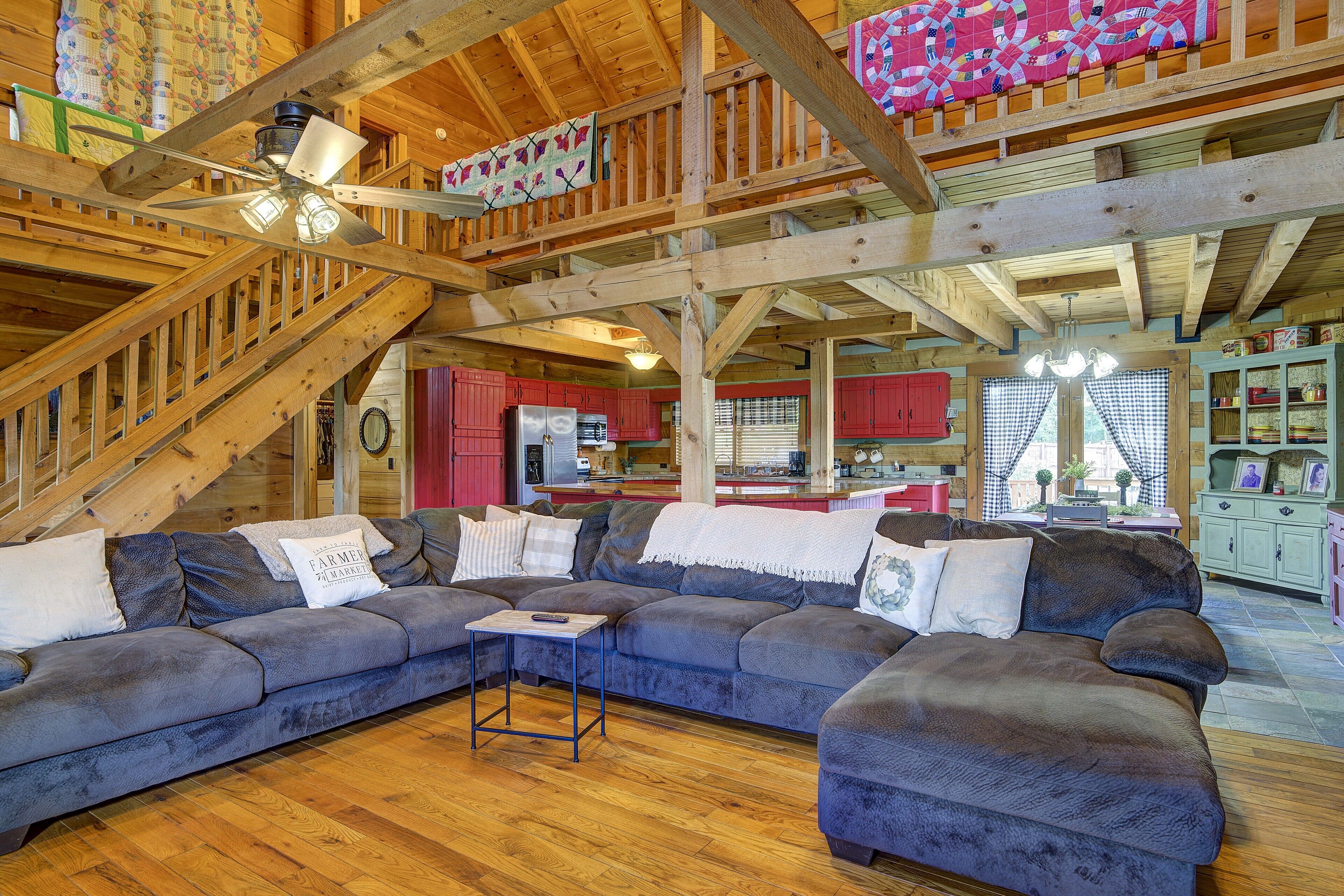 A spacious living area with a large sectional sofa, wooden flooring, and a kitchen in the background.