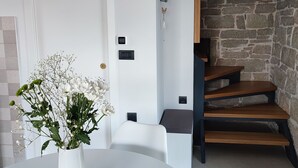 Een modern interieur met een witte deur, een witte tafel met een bloevas, en een trap met houten treden tegen een stenen muur.