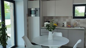 Een moderne keuken met witte kasten, een ingebouwde magnetron en een eethoek met een witte tafel en stoelen.