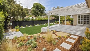 A modern patio with a pergola, a well-maintained lawn, and various plants.