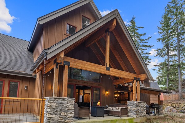A large wooden house with a covered porch, stone pillars, and a fireplace.