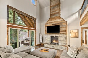 A spacious living room with a stone fireplace, large windows, and a cozy seating area.