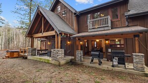 Une cabane en rondins à deux étages, avec des fondations en pierre, une véranda couverte et un espace barbecue.