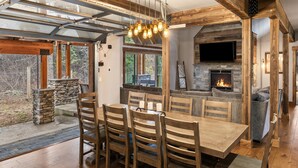 Un coin repas avec des chaises et une table en bois, une cheminée en pierre et un banc en pierre à l’extérieur.
