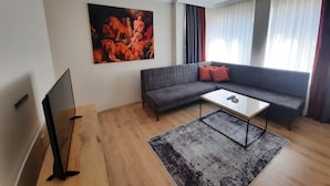 A modern living room with a grey sofa, a coffee table, and a flat-screen TV. - PARK BUTİK (Ankara)