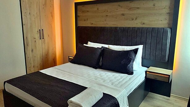 A modern bedroom with a large bed, dark headboard, and a wooden wardrobe. - PARK BUTİK (Ankara)