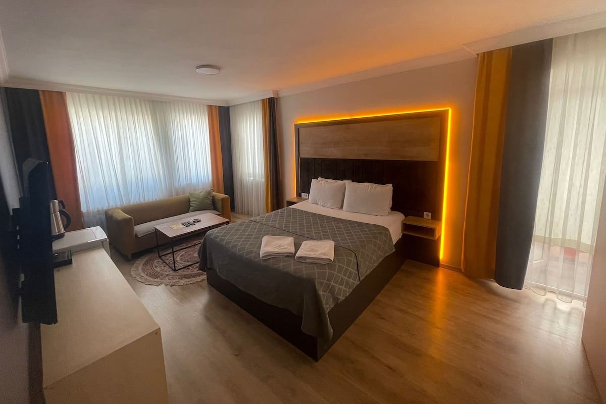 A modern hotel room with a large bed, a sofa, a desk, and a coffee table.