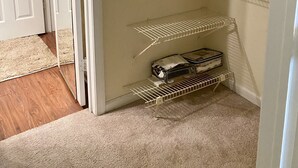 A walk-in closet with a door leading to another room, a shelf with folded towels, and a wire shelf with a suitcase. - The Harmony of Buckhead! (Atlanta)
