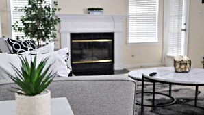 A living room with a grey sofa, a white coffee table, a potted plant, a fireplace, and a round table with a metal frame. - The Harmony of Buckhead! (Atlanta)