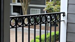 A metal balcony railing with a view of a residential building and a tree with pink flowers. - The Harmony of Buckhead! (Atlanta)