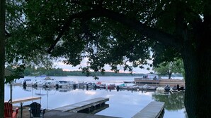 A marina with boats docked, a wooden dock, and a grassy area with chairs.