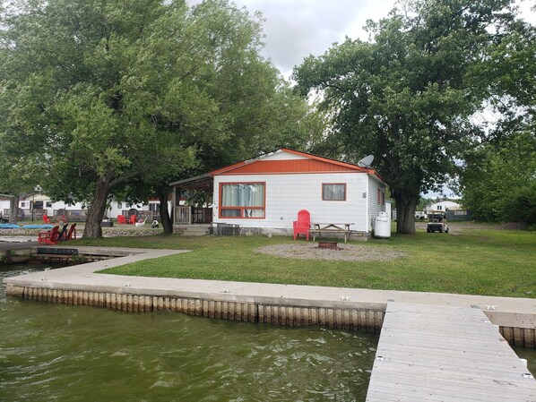 A small white cabin with a red roof, a dock, and a picnic table.