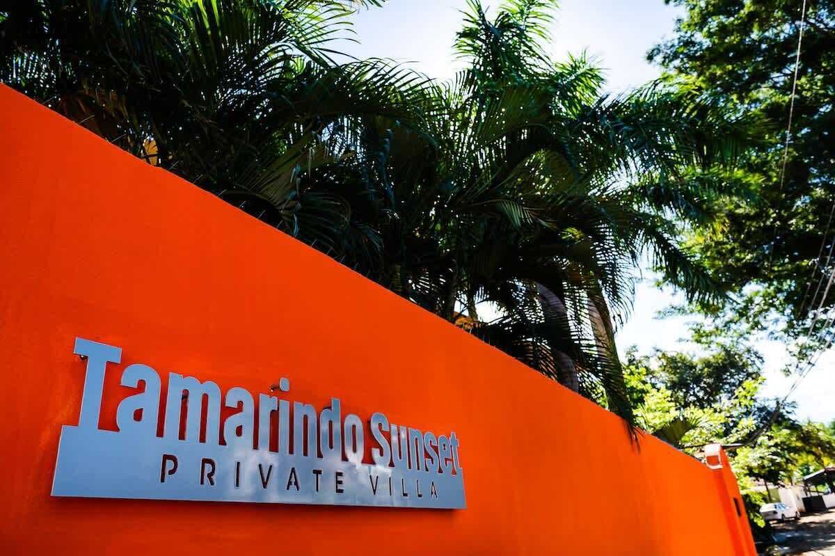 A sign for 'Tamarindo Sunset Private Villa' with a bright orange background and lush green foliage in the background.