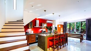 A modern kitchen with a central island, wooden staircase, and large windows offering a view of greenery. - A Tamarindo Sunset (Tamarindo)