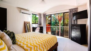 A bedroom with a bed, a TV, a wardrobe, and a balcony with a view of greenery. - A Tamarindo Sunset (Tamarindo)