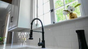 A kitchen with a black faucet, white tiles, and a window with a view of greenery. - Gorgeous home 2mi to LSU - 4 bedroom/3bath (Baton Rouge)