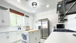A modern kitchen with white cabinetry, a stainless steel refrigerator, and a large island with a sink. - Gorgeous home 2mi to LSU - 4 bedroom/3bath (Baton Rouge)