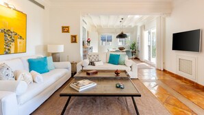 A spacious living room with a white sofa set, a coffee table, and a TV mounted on the wall.