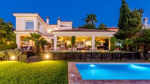 A large, modern house with a swimming pool, surrounded by well-maintained lawns and tropical plants.