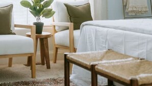 A room with a bed, two chairs, a small table with a plant, a mirror, and a window with curtains. - The Congaree Cottage (Cayce)