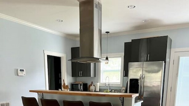 A modern kitchen with a central island, bar stools, a stainless steel refrigerator, and a built-in oven. - The Congaree Cottage (Cayce)