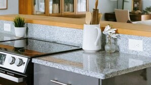 A modern kitchen with a gas stove, granite countertop, wooden cabinets, and a ceiling fan. - The Congaree Cottage (Cayce)