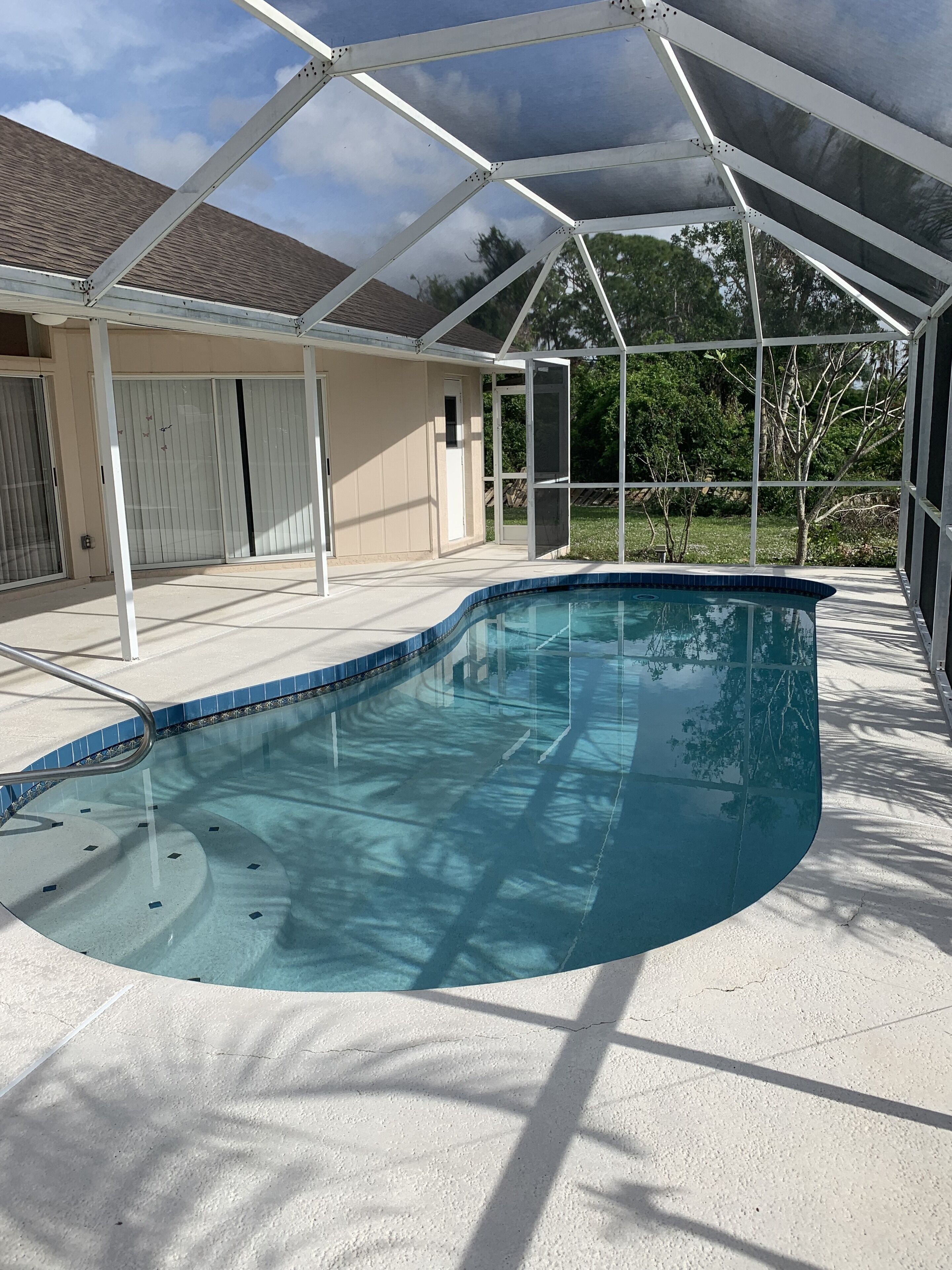 A covered outdoor swimming pool with a curved design, surrounded by a white fence and a house with a beige exterior.