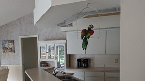 Ett modernt kök med en stor köksö, vita skåp och en hängande, dekorativ fågel.